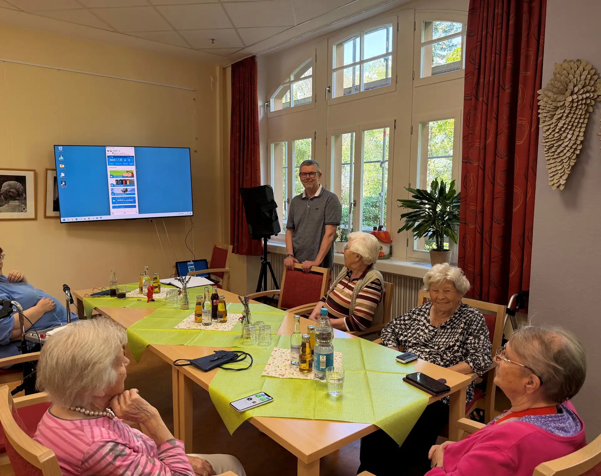 Seniorinnen und Senioren hören einem Kursleiter beim Smartphone-Umgang zu; im Vordergrund sind Smartphones zu sehen.