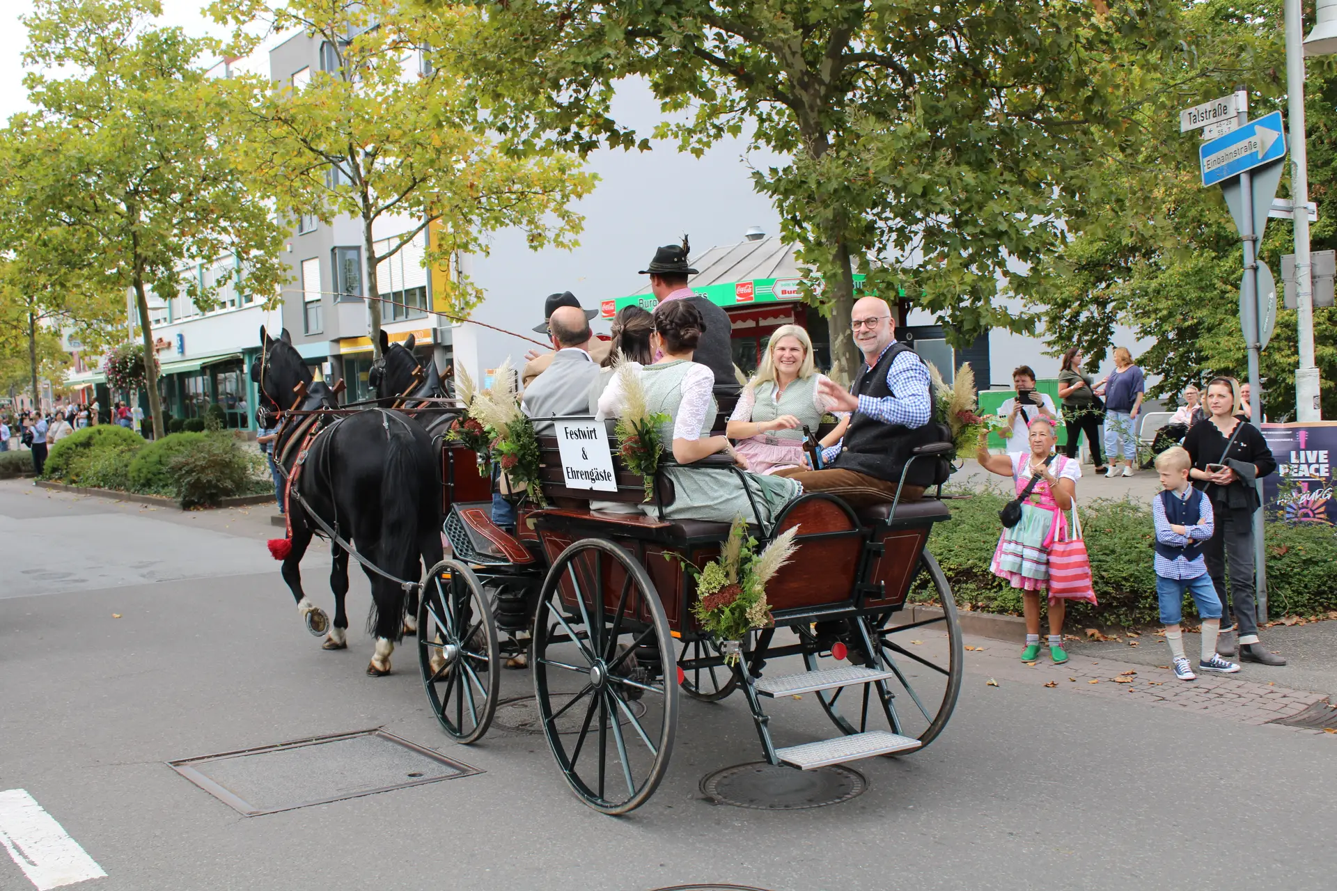Oberbürgermeister Michael Forster und Bürgermeister Manfred Rippel sitzen auf einer Kutsche bei einem Umzug zur Wiesn; die Personen befinden sich auf der Kutsche vorn und hinten, von zwei Pferden gezogen.